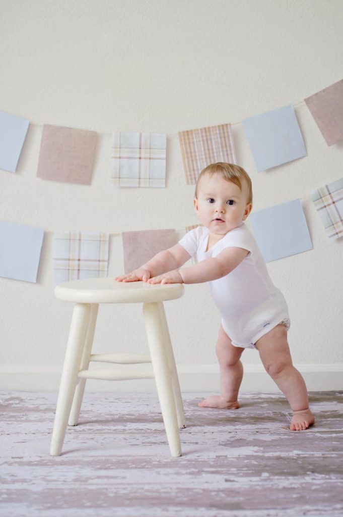 pexels-photo-459976 Cute baby standing by a stool indoors with a playful background.