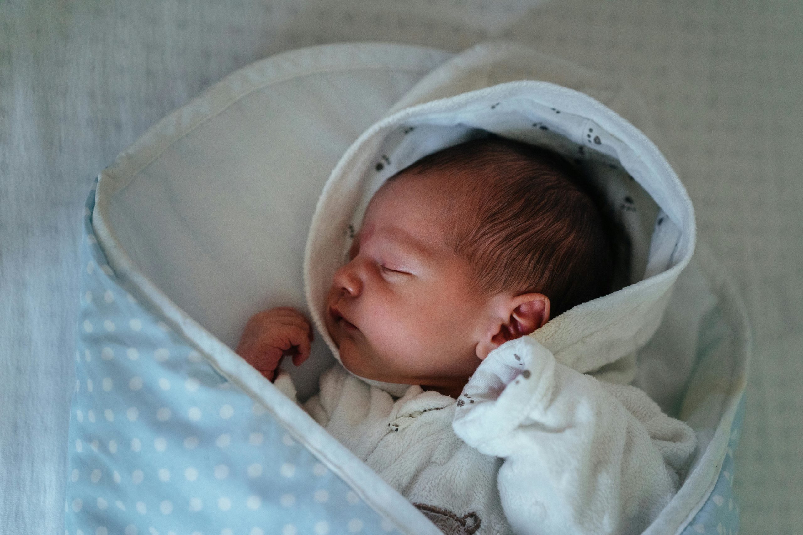 A serene newborn baby peacefully sleeping in a cozy, blue polka dot blanket indoors.
